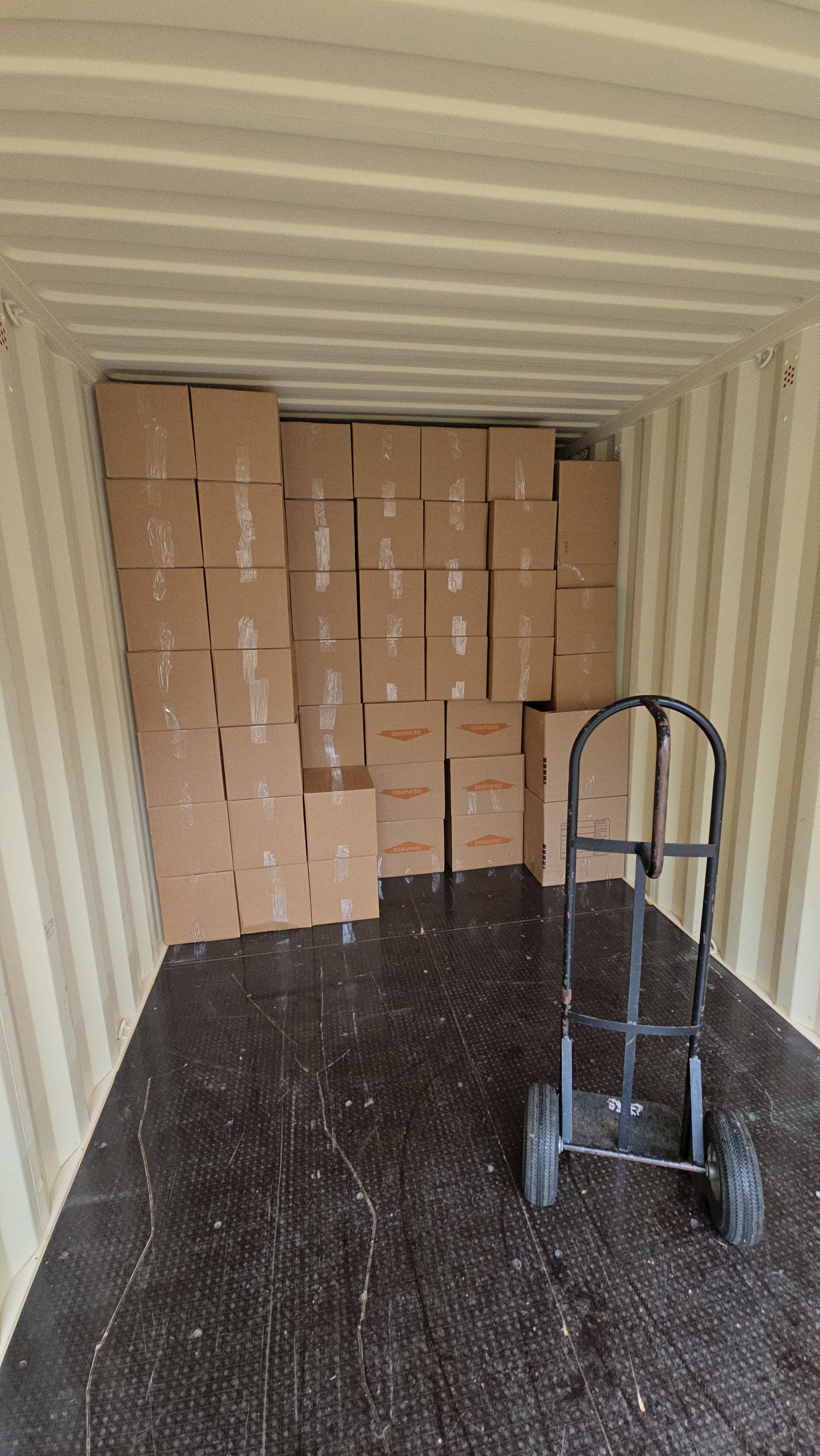 A wall of cardboard boxes at the back of a loaded truck, hand truck in front