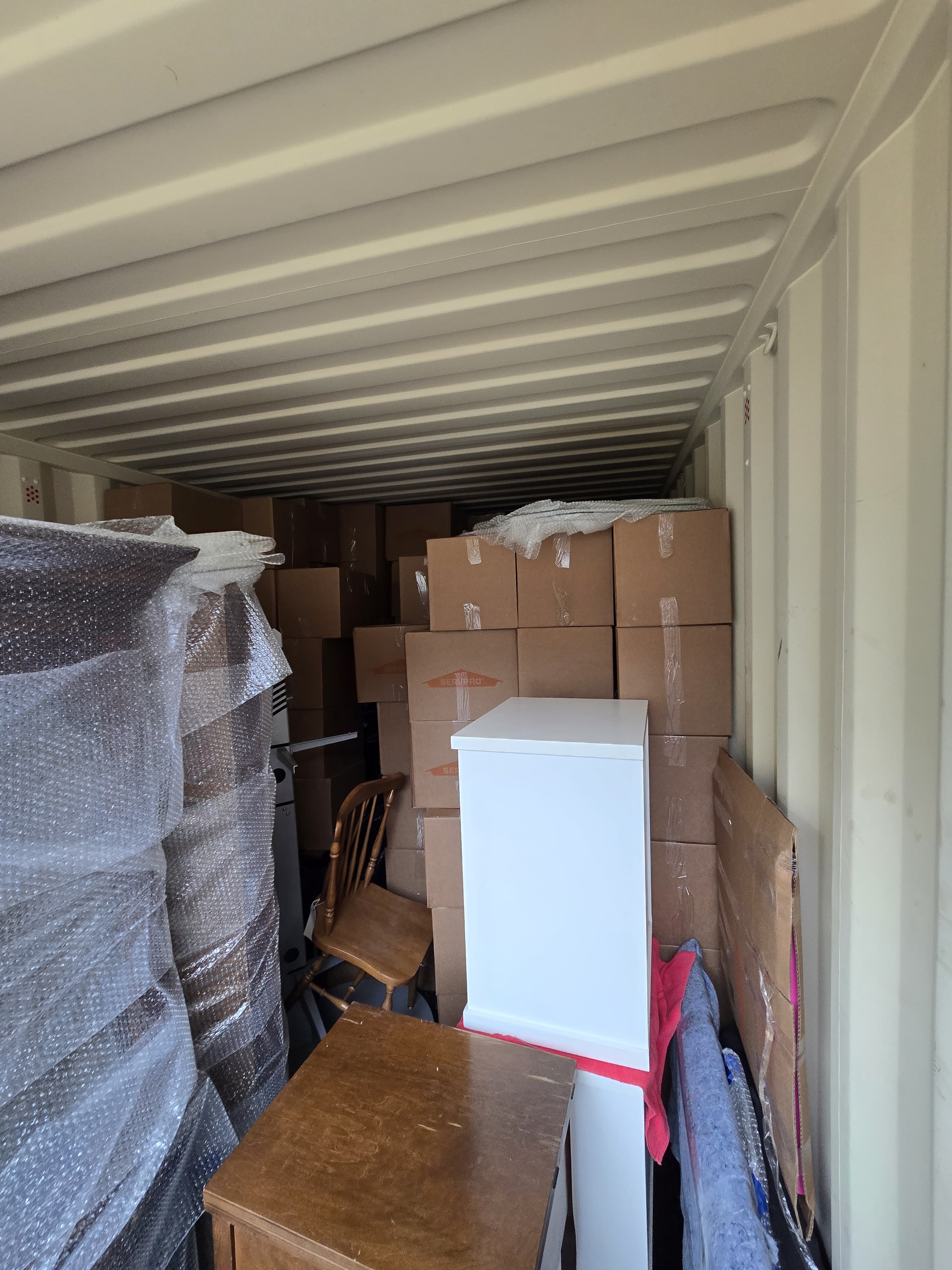 A storage container packed with boxes, a white cabinet and bubble-wrapped furniture