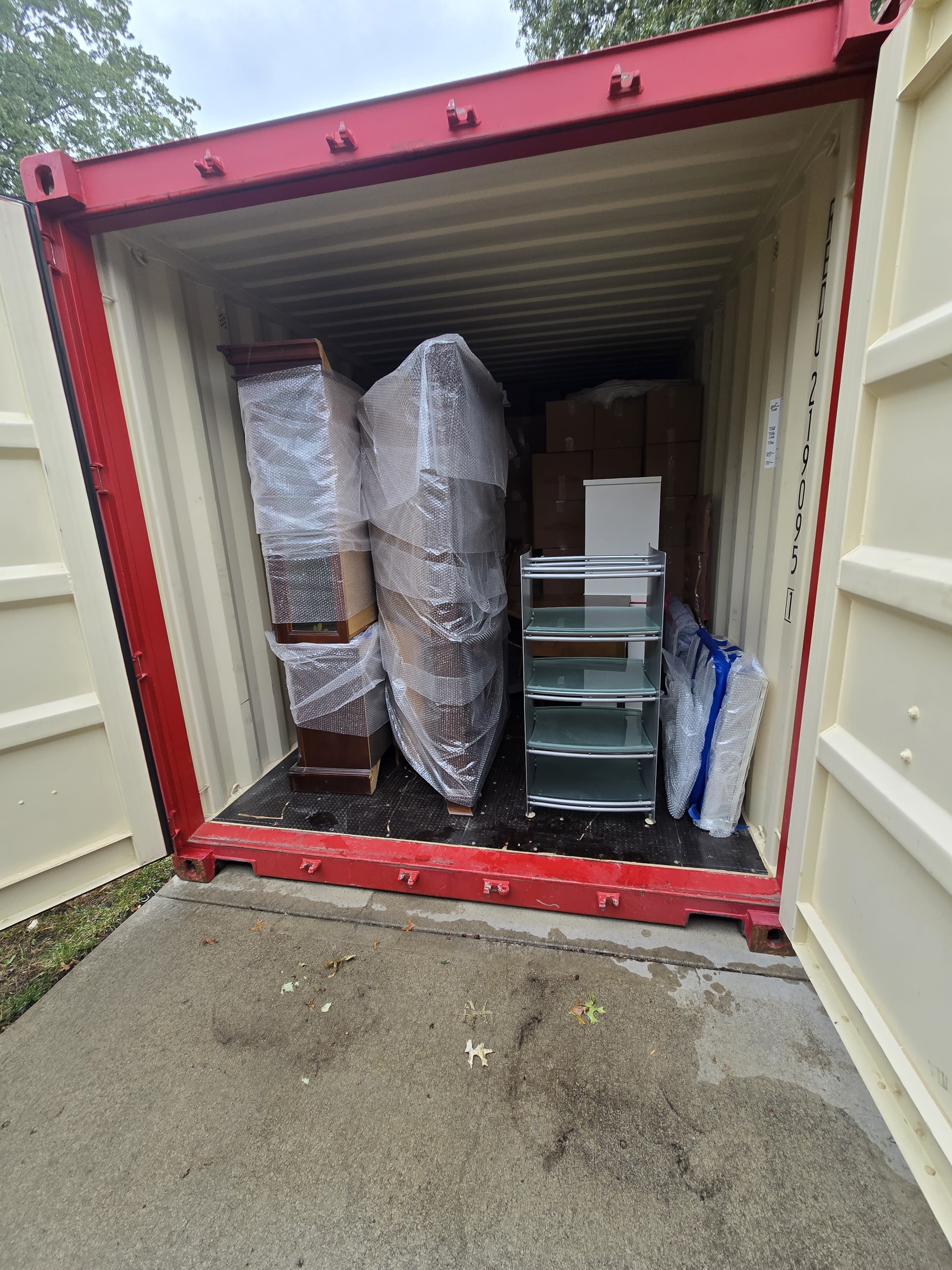 An open shipping container packed with wrapped furniture, boxes and a glass shelf