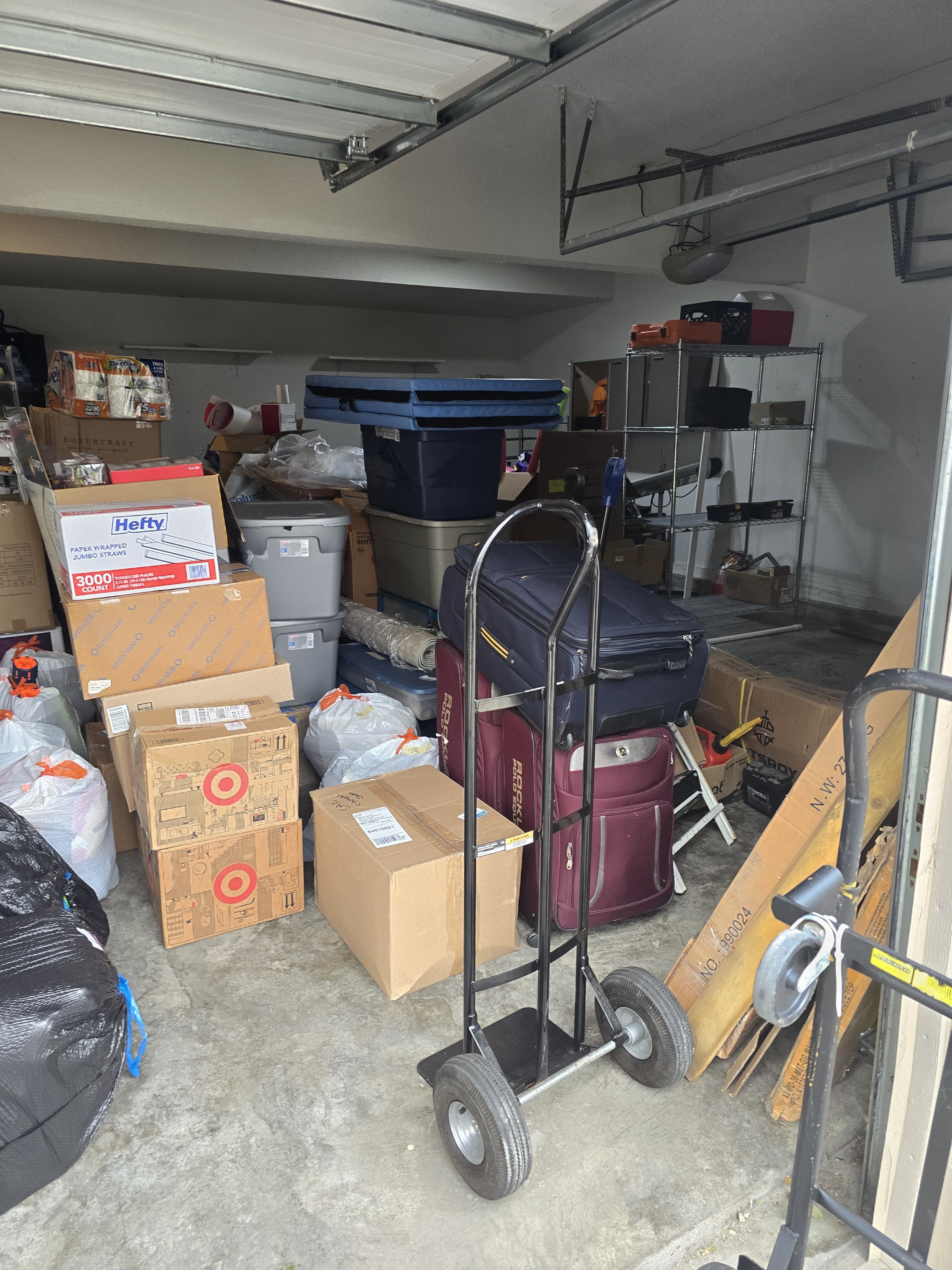 A garage packed for a move, luggage stacked on a hand truck