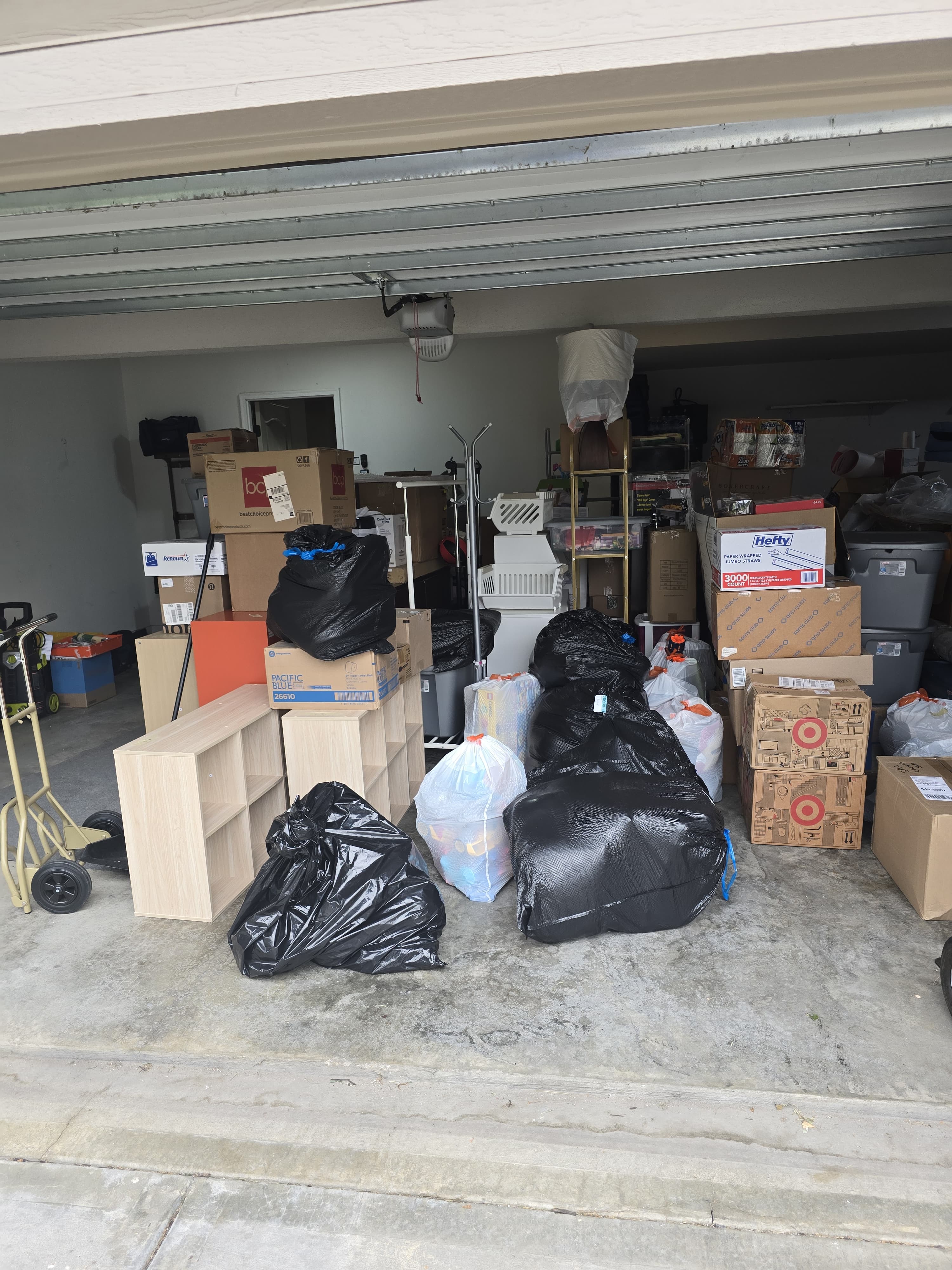 A garage lined with boxes, totes and bagged bedding, hand truck at the door