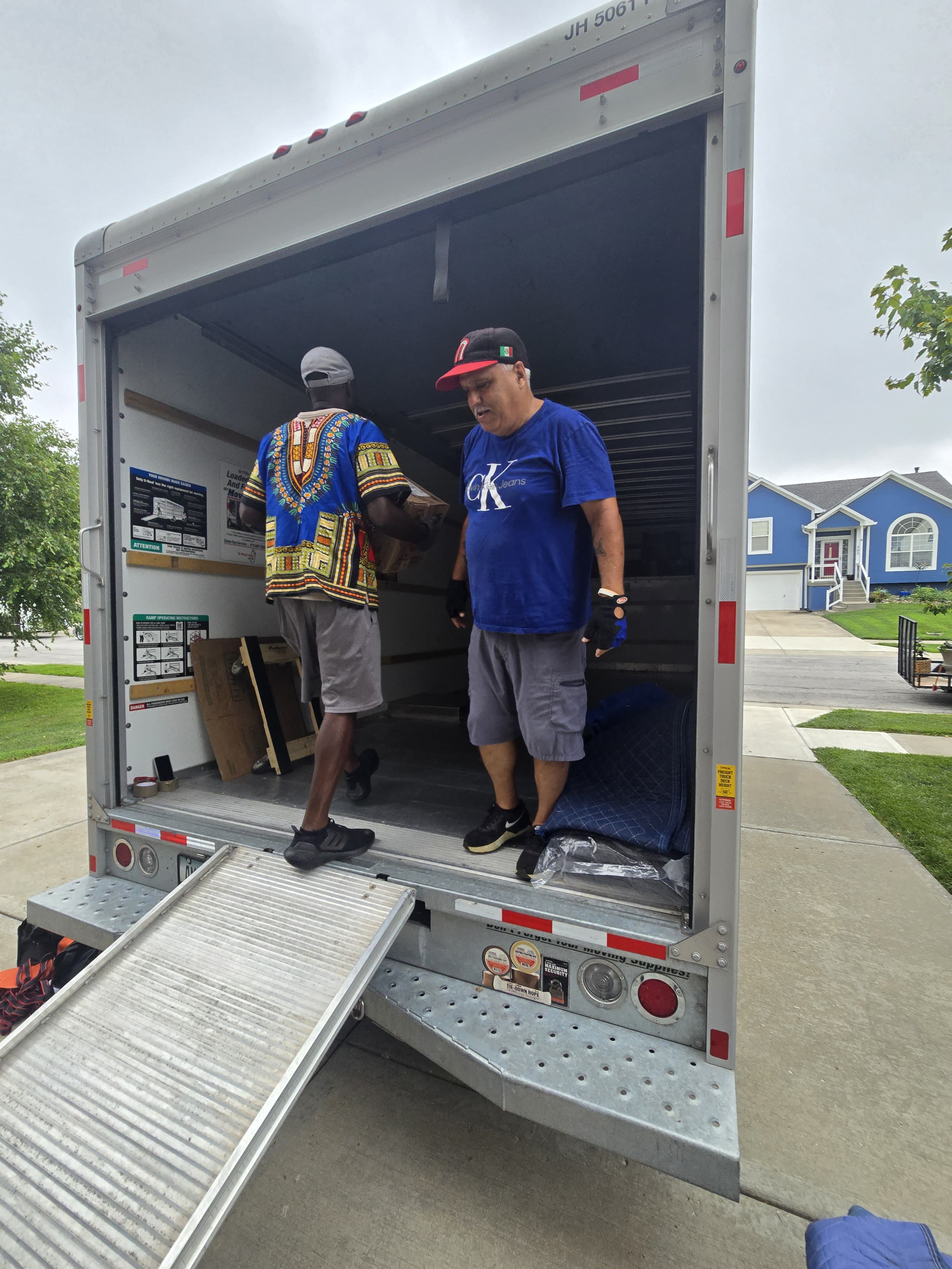 Two movers loading boxes at the back of a truck on a residential driveway