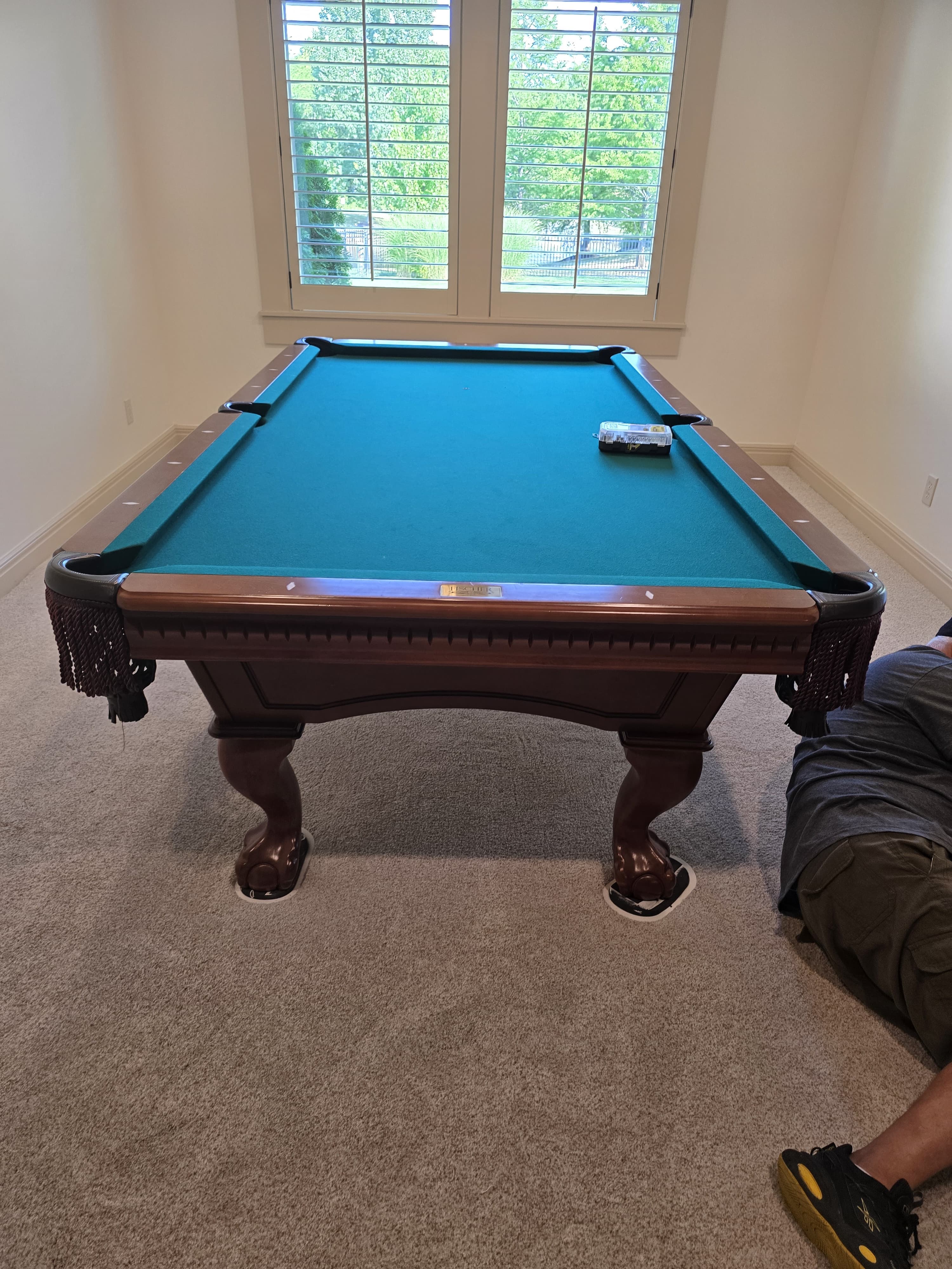 A claw-foot pool table on sliders after reassembly, hardware box on the felt